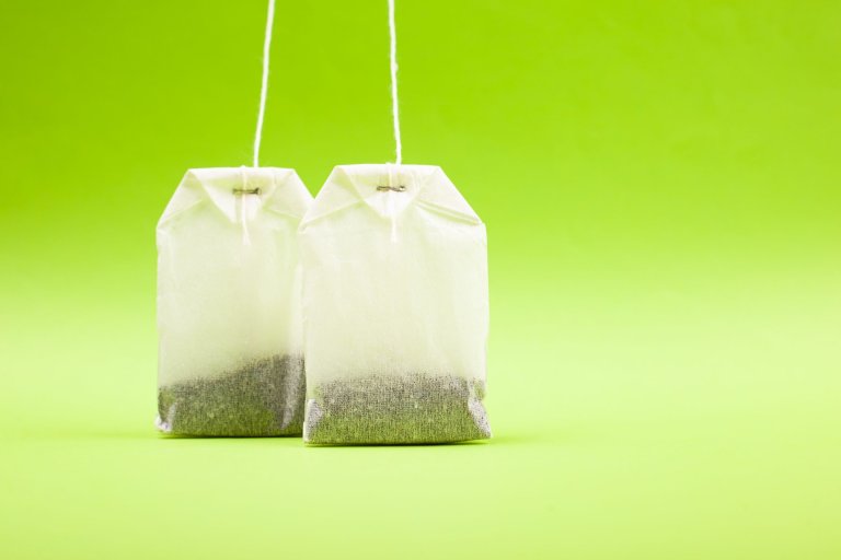 two-white-paper-bags-with-black-tea-light-green-background-copy-space-close-up