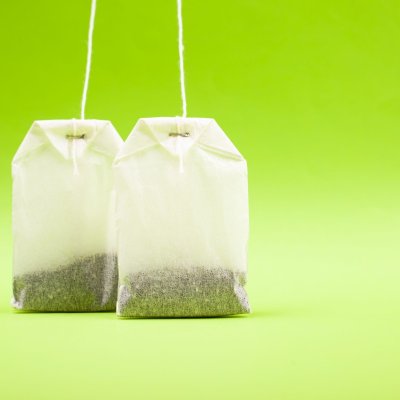 two white paper bags with black tea on a light green background copy space, close-up