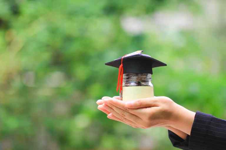 Woman hand holding coins money in glass bottle with graduates ha